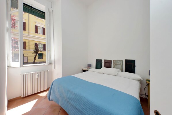 A bedroom with a bed, a window, a radiator, and a nightstand. - 4BNB - Quiriti Delightful Apartment (Roma)