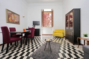 A dining area with a checkered floor, a table with chairs, a television, and a window with autumn leaves. - 4BNB - Quiriti Delightful Apartment (Roma)