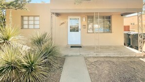 A building with a beige exterior, a white door, and a small window. There is a number '444' on the wall and a metal gate to the right. - Pet Friendly! Private Casita in Nob Hill (Albuquerque)