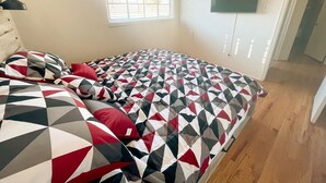 A bedroom with a bed covered in a geometric patterned bedspread, a window with blinds, and a flat-screen TV mounted on the wall. - Pet Friendly! Private Casita in Nob Hill (Albuquerque)