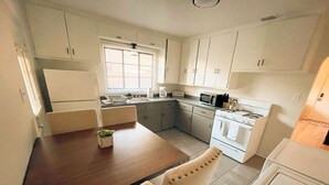 A compact kitchen with white cabinets, a dining table with chairs, a microwave, a stove, and a refrigerator. - Pet Friendly! Private Casita in Nob Hill (Albuquerque)