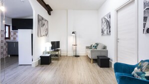 Una sala de estar con un sofá gris, un sillón azul, una lámpara de pie y obras de arte en las paredes.