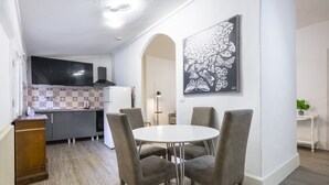 Una cocina moderna con comedor, que incluye una mesa redonda con sillas, una obra de arte blanco y negro en la pared y un armario blanco con un salpicadero decorativo.