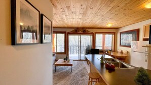 A modern kitchen with wooden ceiling, large windows, and a dining area with a sofa and coffee table. - Apex Mountain ~ Mountain Tranquility (Hedley)
