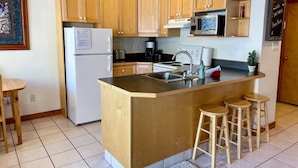A compact kitchen with wooden cabinets, a central island with stools, a refrigerator, a microwave, and a stove. - Apex Mountain ~ Mountain Tranquility (Hedley)