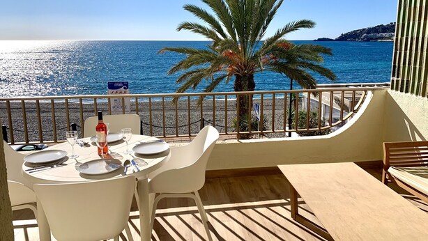 A balcony with a table set for dining, overlooking a beach and the sea. - NEW APARTAMENT WITH LARGE TERRACE JUST ON THE BEACH W/ FAST  INTERNET (Almuñécar)