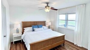 Ein Schlafzimmer mit einem hölzernen Bett, weißen Wänden, einem Deckenventilator und einem Fenster mit Vorhängen.