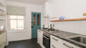 A compact kitchen with a teal door, a gas stove, and a sink. - Bluebell Apartment (Swanage)