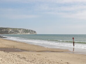 A beach with a cliff in the background, a red sign, and a wooden structure near the water. - Bluebell Apartment (Swanage)