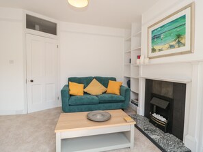 A living room with a teal sofa, a fireplace, and a painting above it. - Bluebell Apartment (Swanage)
