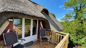 A thatched-roof building with a wooden deck and two chairs. - la Fontaine Romy (Genneville)