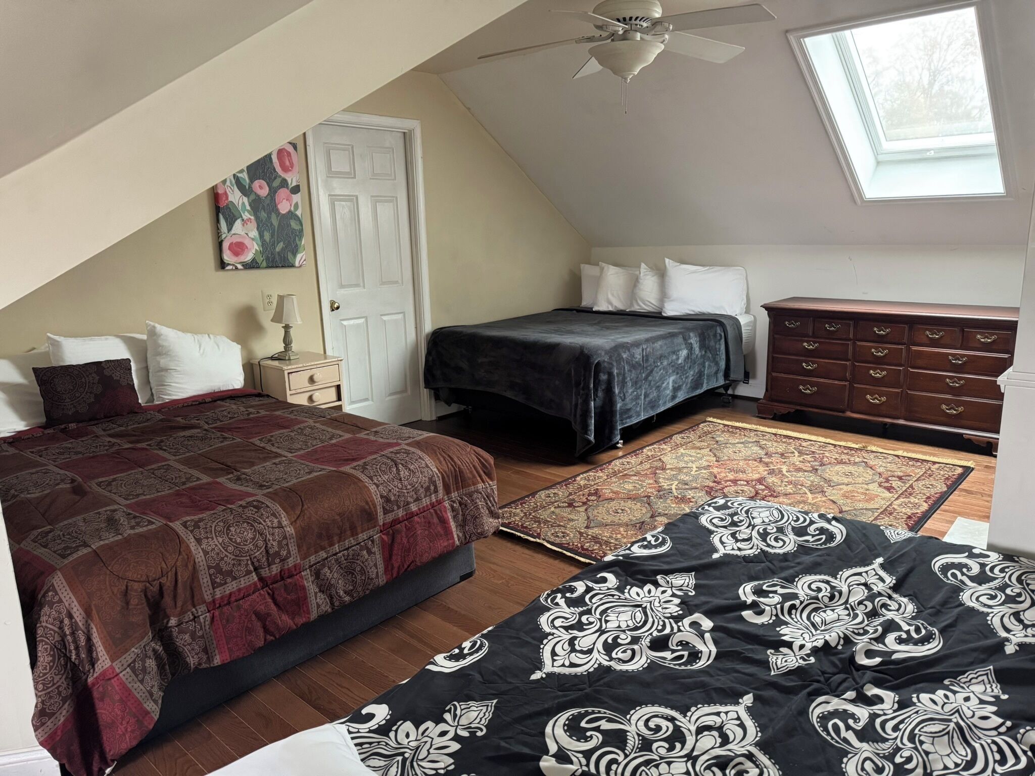 Une chambre avec un plafond en pente, un lit recouvert d’une couvre-lit à motifs, une commode et un puits de lumière.