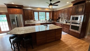 A spacious kitchen with wooden cabinets, stainless steel appliances, and a large island with bar stools. - Large Home w/ Private Pool, Gym, Sauna, 7 Bedrooms, Sleeps 21 (Severn)