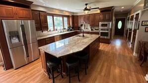 A spacious kitchen with wooden cabinets, stainless steel appliances, a large island with stools, and a ceiling fan. - Large Home w/ Private Pool, Gym, Sauna, 7 Bedrooms, Sleeps 21 (Severn)