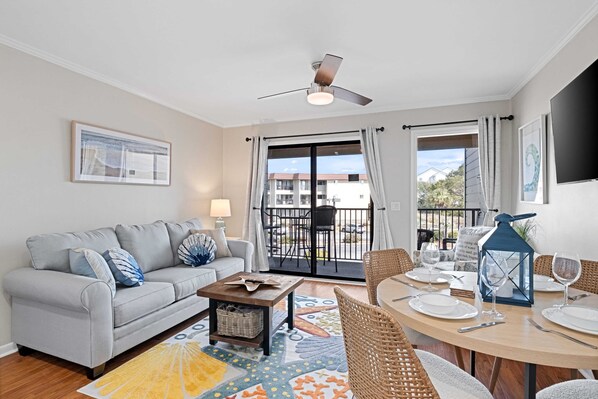 A living room with a sofa, coffee table, and dining area with chairs and a table set for dining.