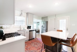 Una cocina moderna con armarios blancos, una estufa a gas, un refrigerador y un comedor con mesa y sillas.