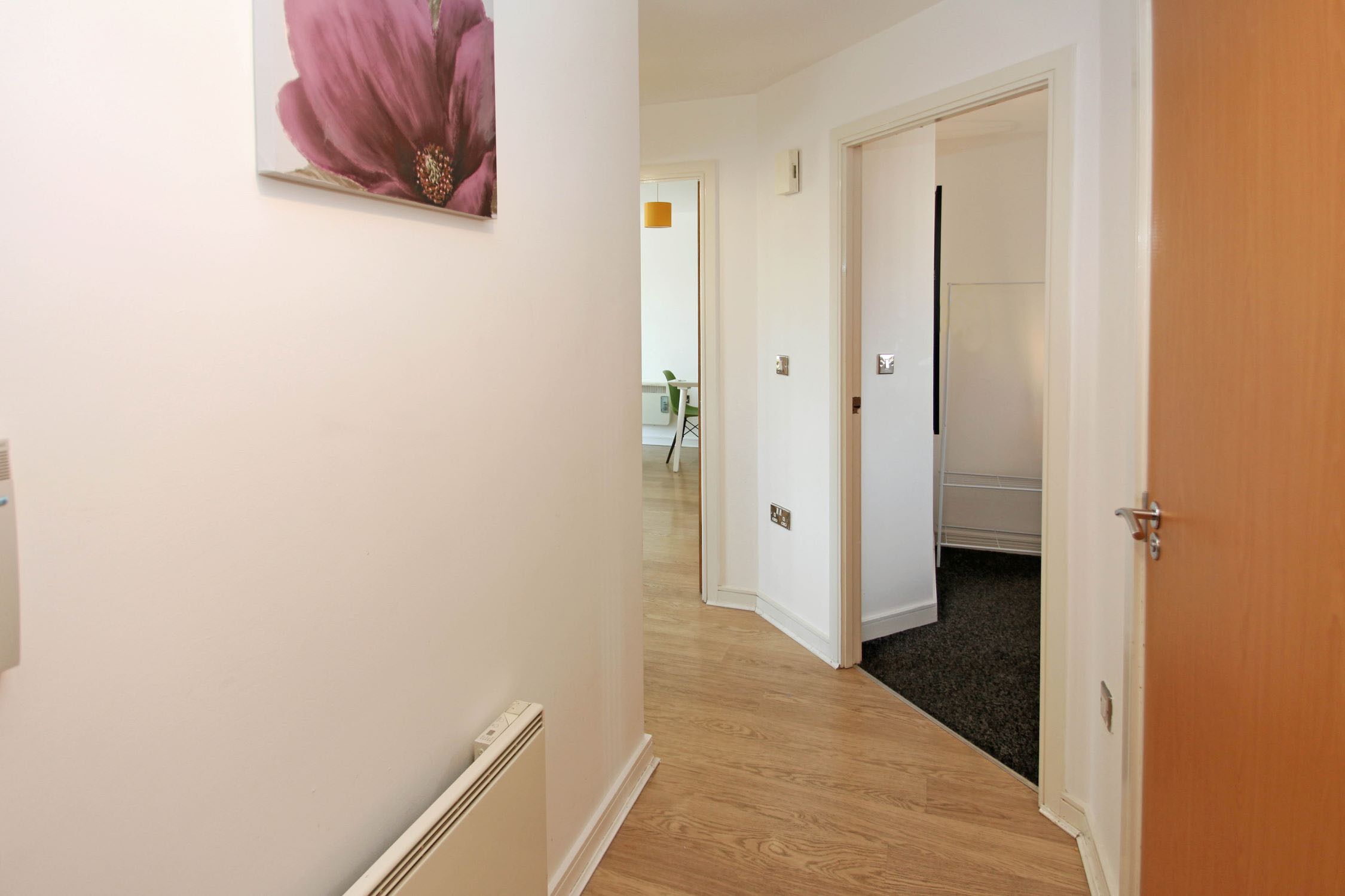 A hallway with a wooden floor, white walls, and a door leading to another room.