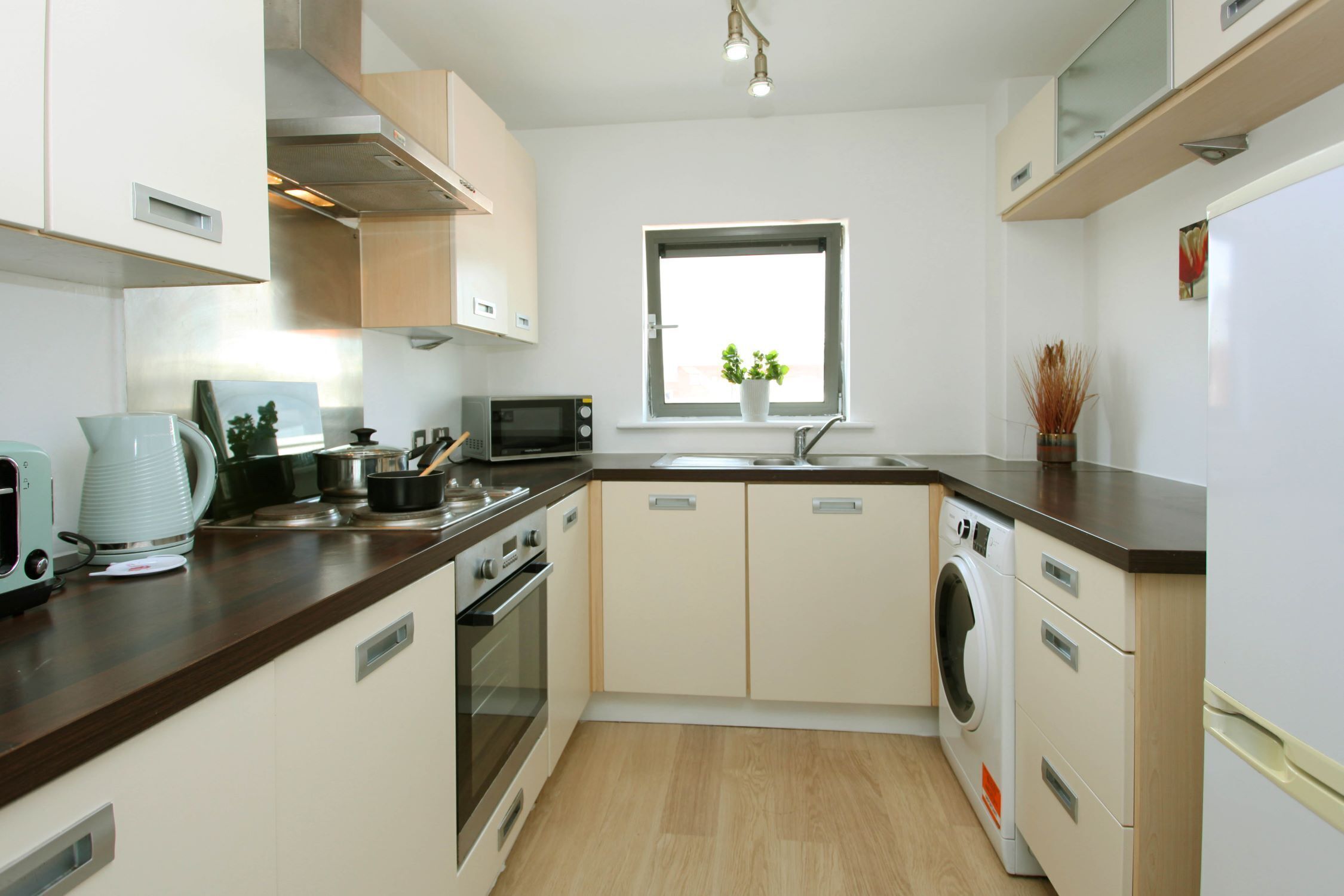 A compact kitchen with a microwave, toaster, sink, and a washing machine.