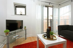 Una sala de estar moderna con un televisor de pantalla plana, una mesa de centro de vidrio, una alfombra roja y un sofá negro.