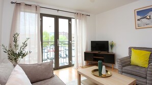 A modern living room with a sofa, a coffee table, a TV on a stand, and a balcony with a view of the city. - Albion Street Apartments (Wolverhampton)