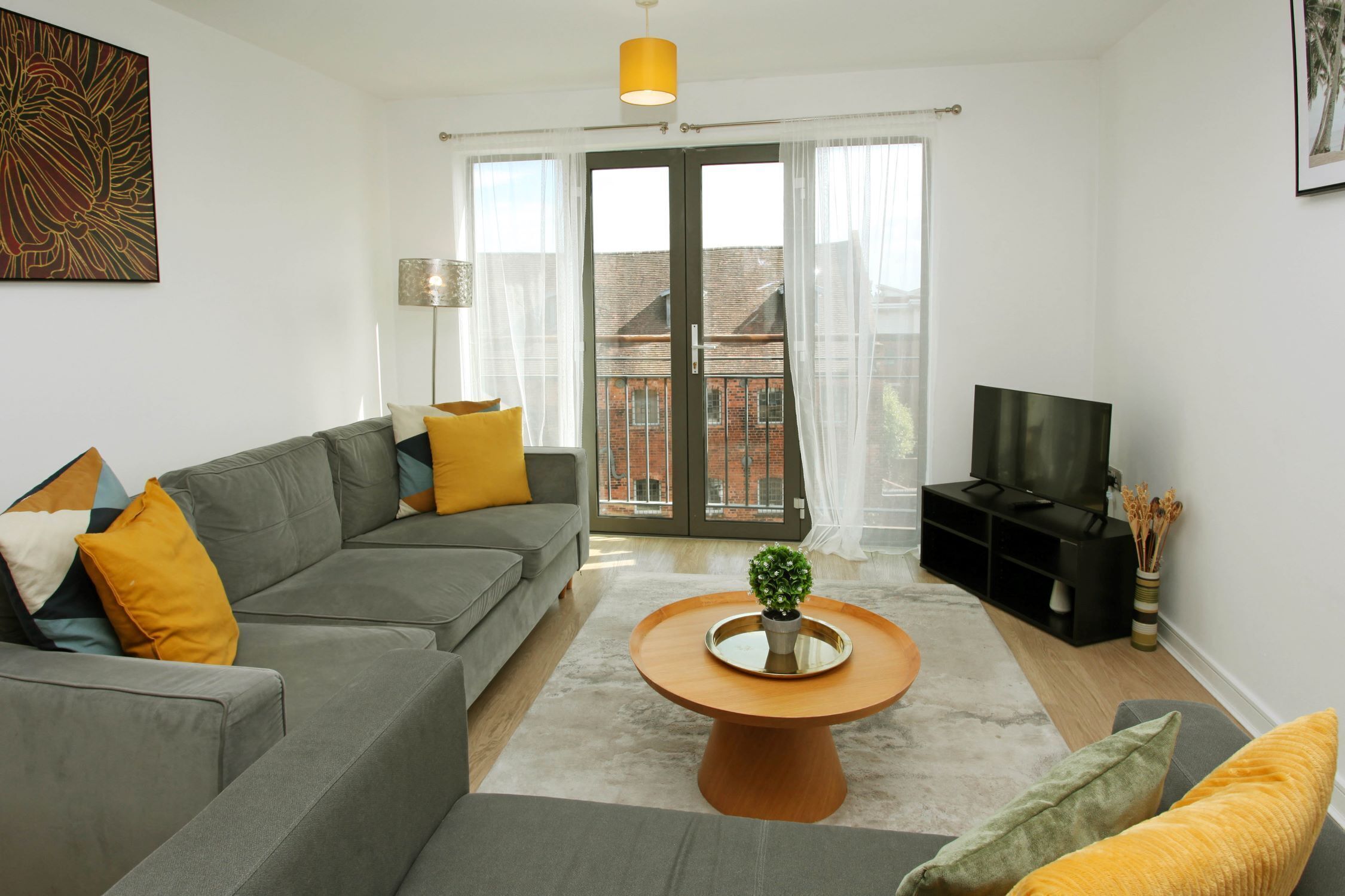 A modern living room with a grey sofa, a round wooden coffee table, and a television on a black stand.