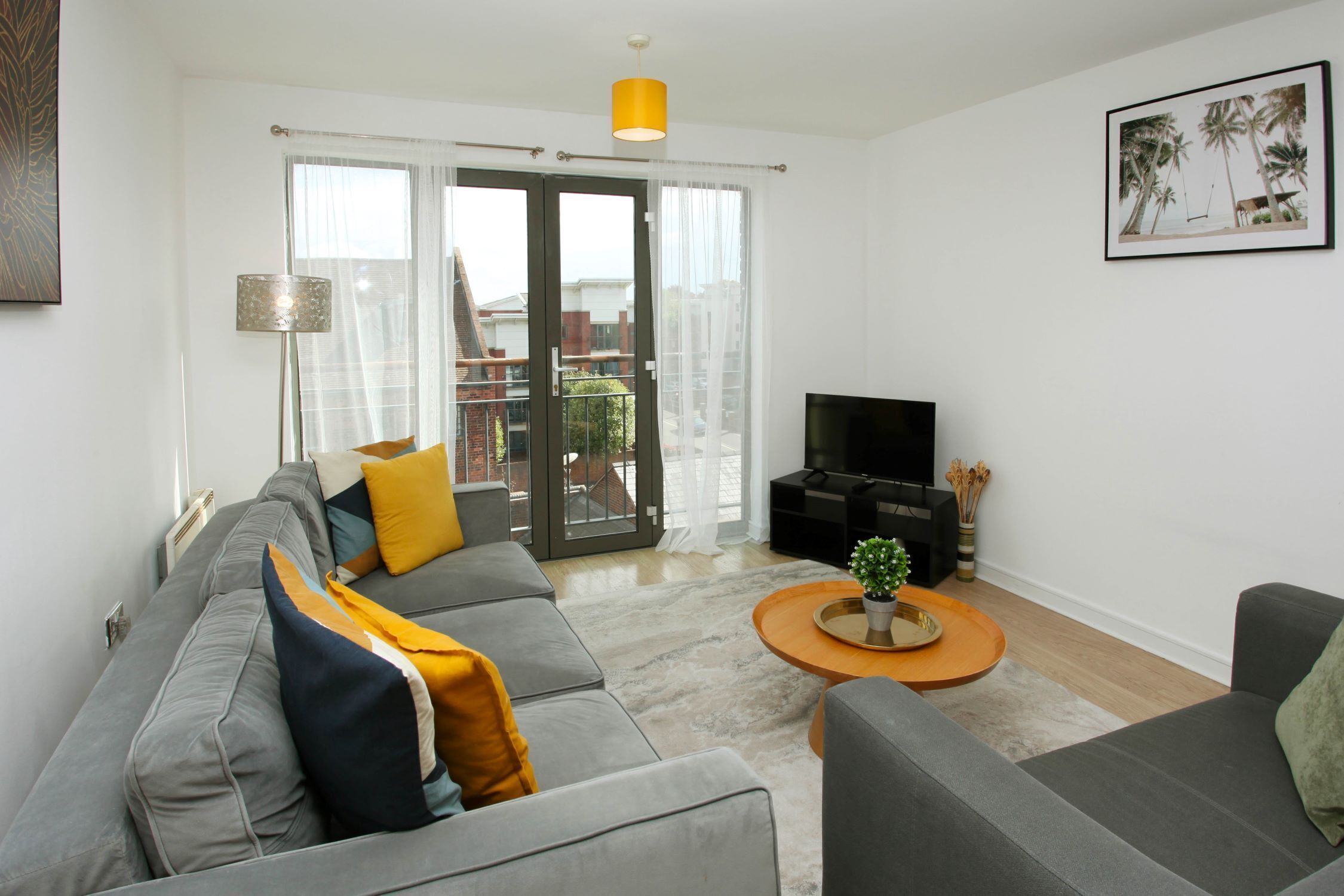 Una sala de estar moderna con un sofá gris, una mesa de centro con una planta y un televisor de pantalla plana.