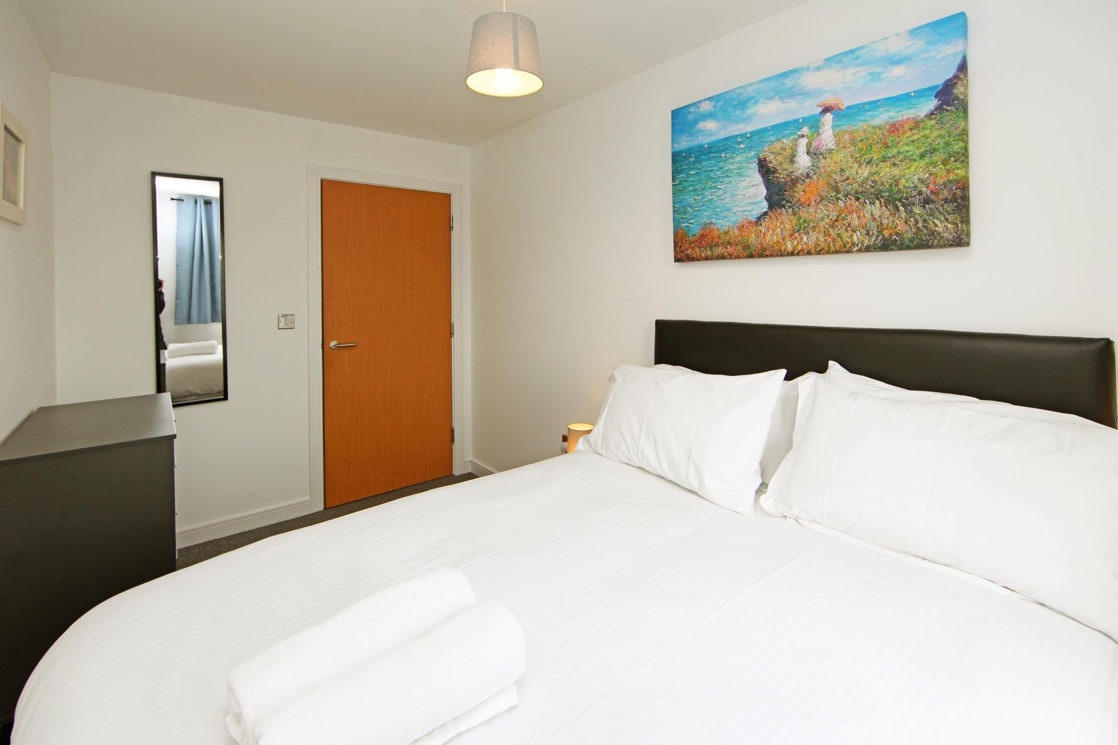 Une chambre d’hôtel avec un lit, un bureau, une porte et un tableau au mur.