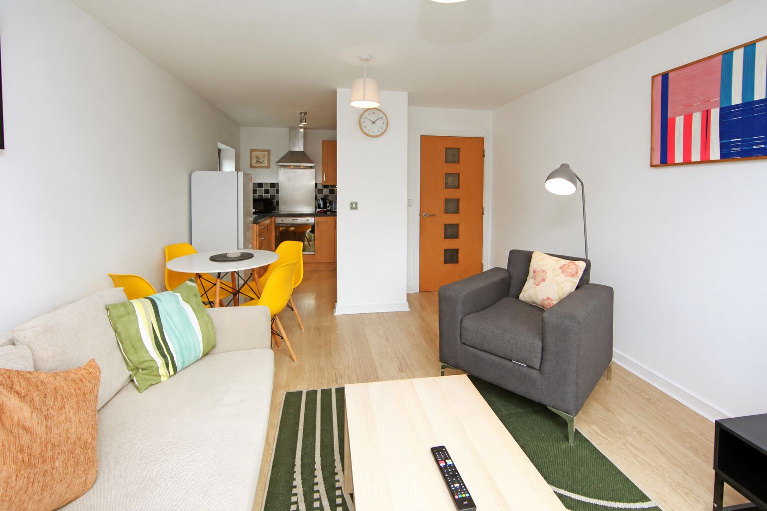En stue med en sofa, en grå lænestol, et sofabord og et spiseområde med gule stole.