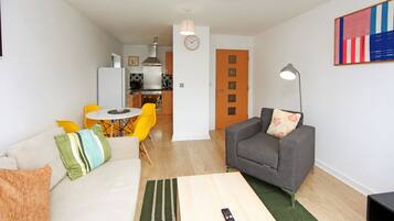 En stue med en sofa, en grå lænestol, et sofabord og et spiseområde med gule stole.