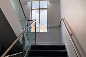 A modern staircase with glass railings and a view of the outside through a large window. - Albion Street Apartments (Wolverhampton)