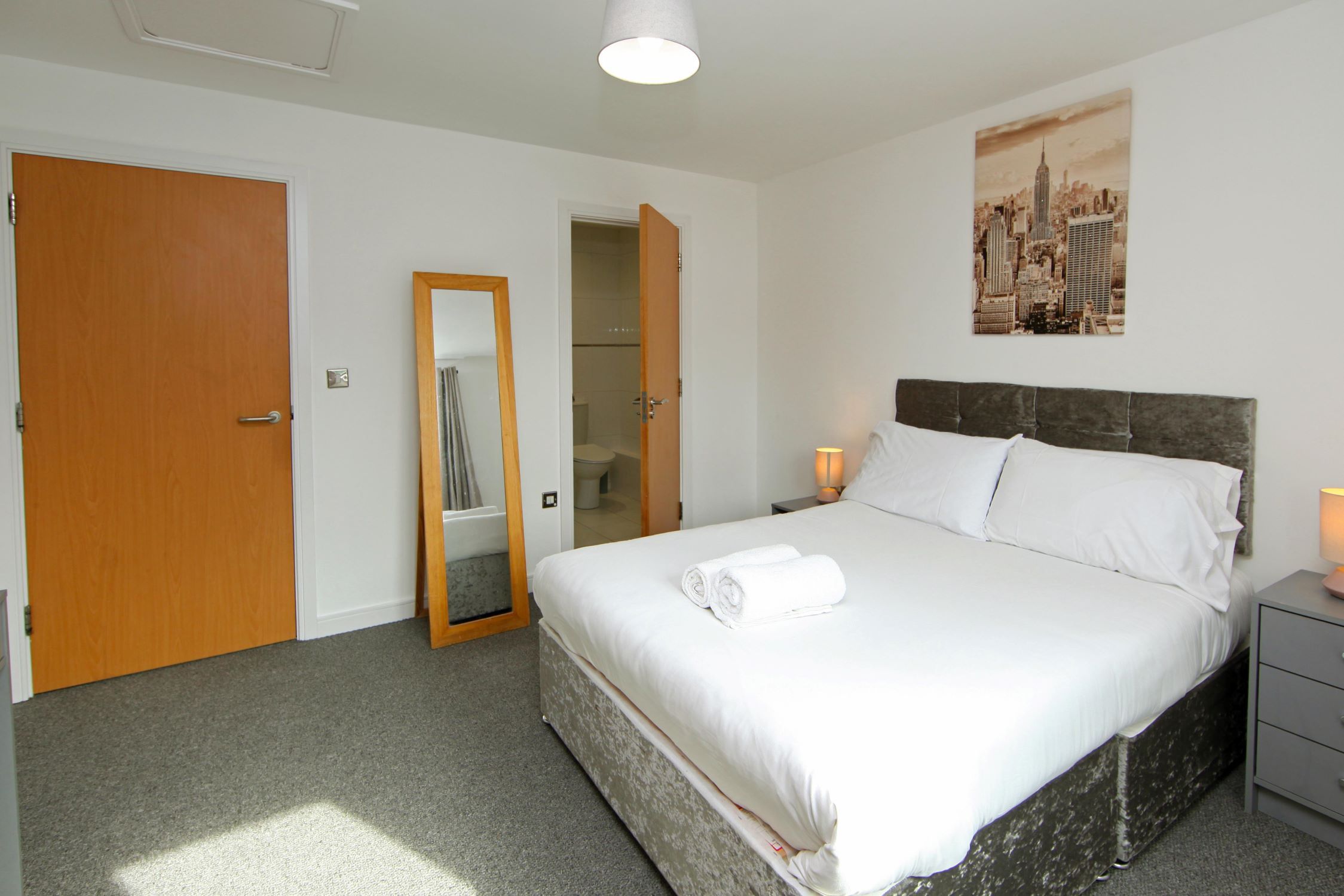 Une chambre d’hôtel avec un lit, une table de chevet, un miroir et une porte.