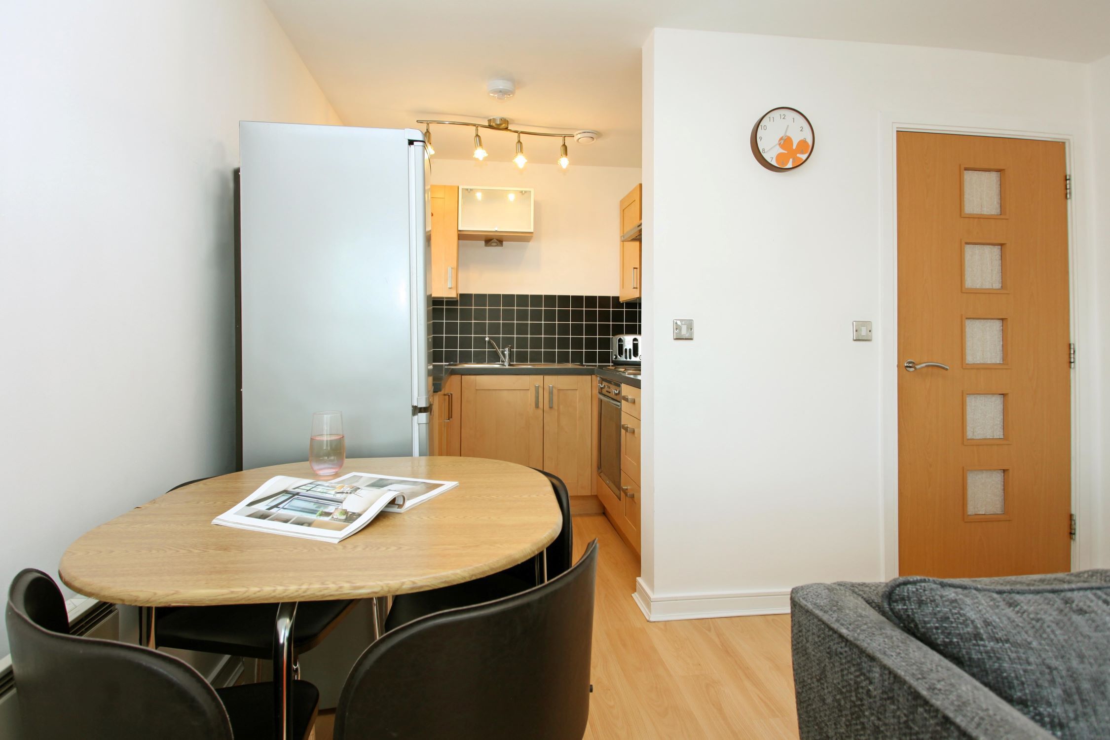 A compact kitchen with a dining area, a refrigerator, a sink, and a clock on the wall.