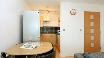 A compact kitchen with a dining area, a refrigerator, a sink, and a clock on the wall.