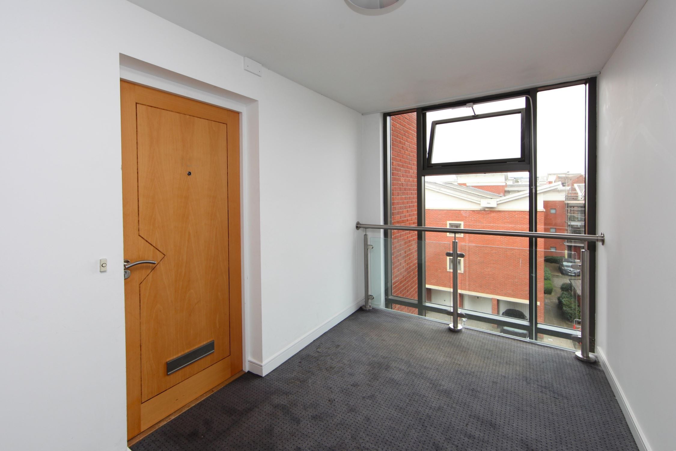 Una habitación con puerta de madera, barandilla de balcón de vidrio y vistas a edificios.