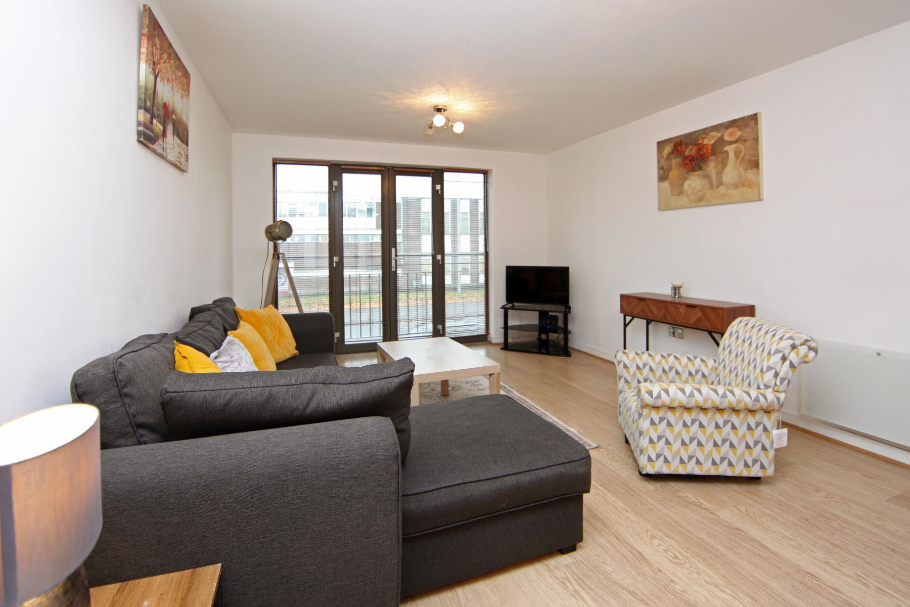 A modern living room with a grey sofa, a patterned armchair, a small table, and a TV.