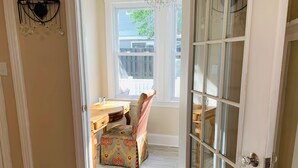 A room with a wooden desk, a patterned chair, and a window with a view of a fence and trees. - Family-Sized with Bay Views and Close to Beach (Ventnor City)