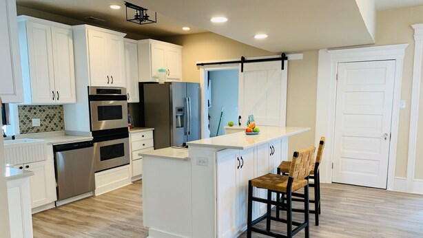 A modern kitchen with white cabinetry, stainless steel appliances, a central island, and a dining area with two chairs. - Family-Sized with Bay Views and Close to Beach (Ventnor City)