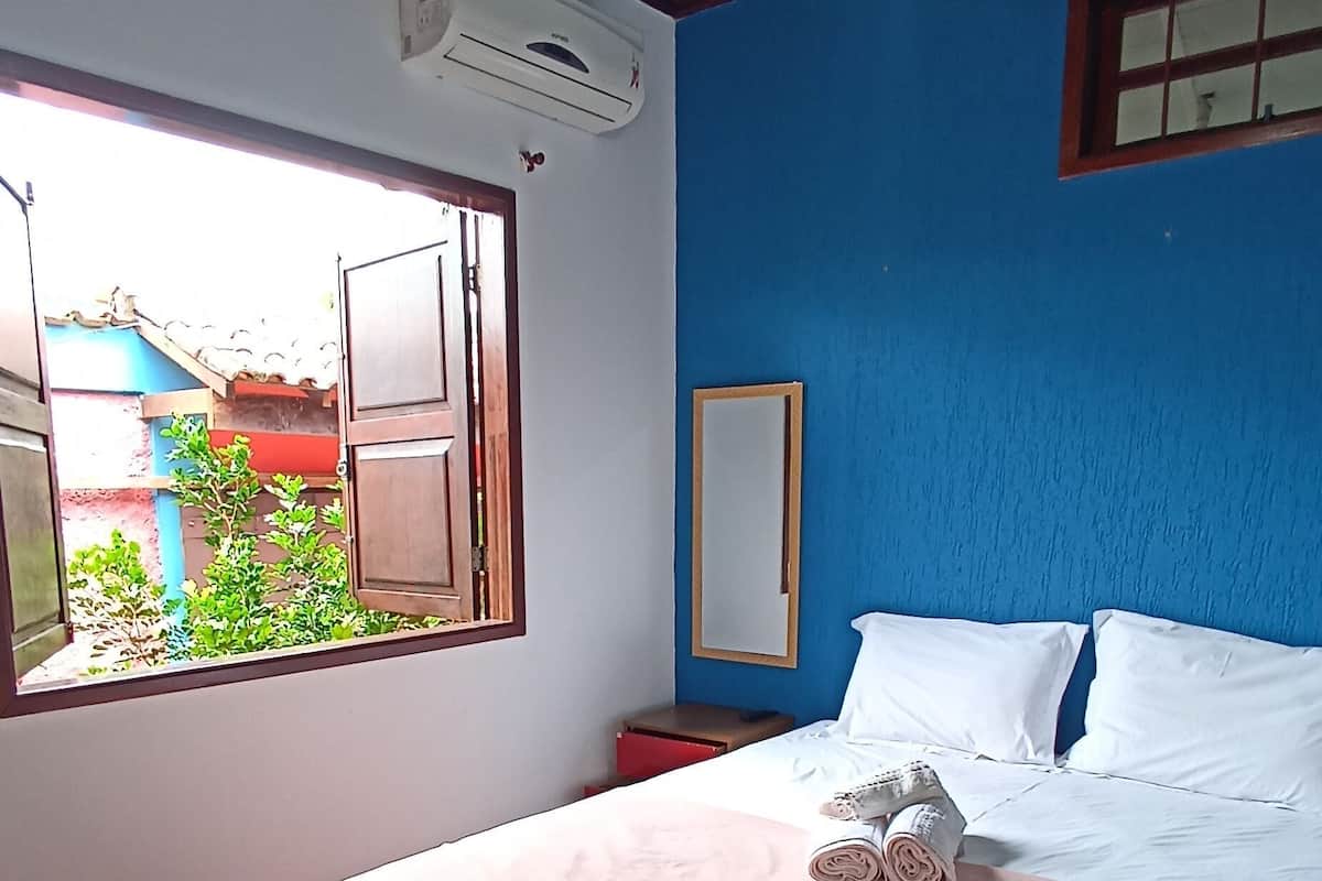 A bedroom with a bed, a desk, a chair, a window, a ceiling fan, and an air conditioning unit.