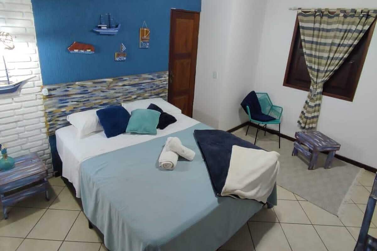 A bedroom with a bed, a ceiling fan, a window with curtains, a chair, and a small table.
