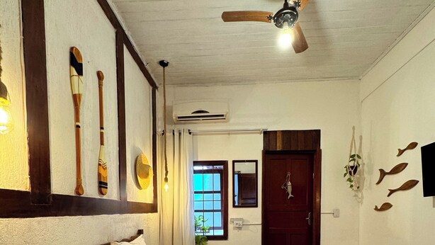 Une chambre à coucher avec un lit, un ventilateur de plafond, un banc en bois et une petite table.
