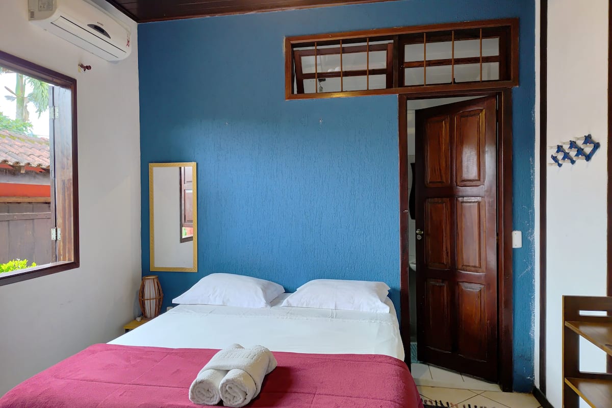 A room with a bed, a window, a door, and a wall-mounted air conditioner.