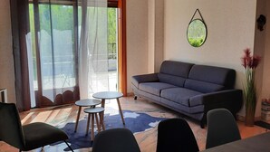Ett modernt vardagsrum med en soffa, fåtöljer, ett matbord och utsikt genom ett stort fönster.