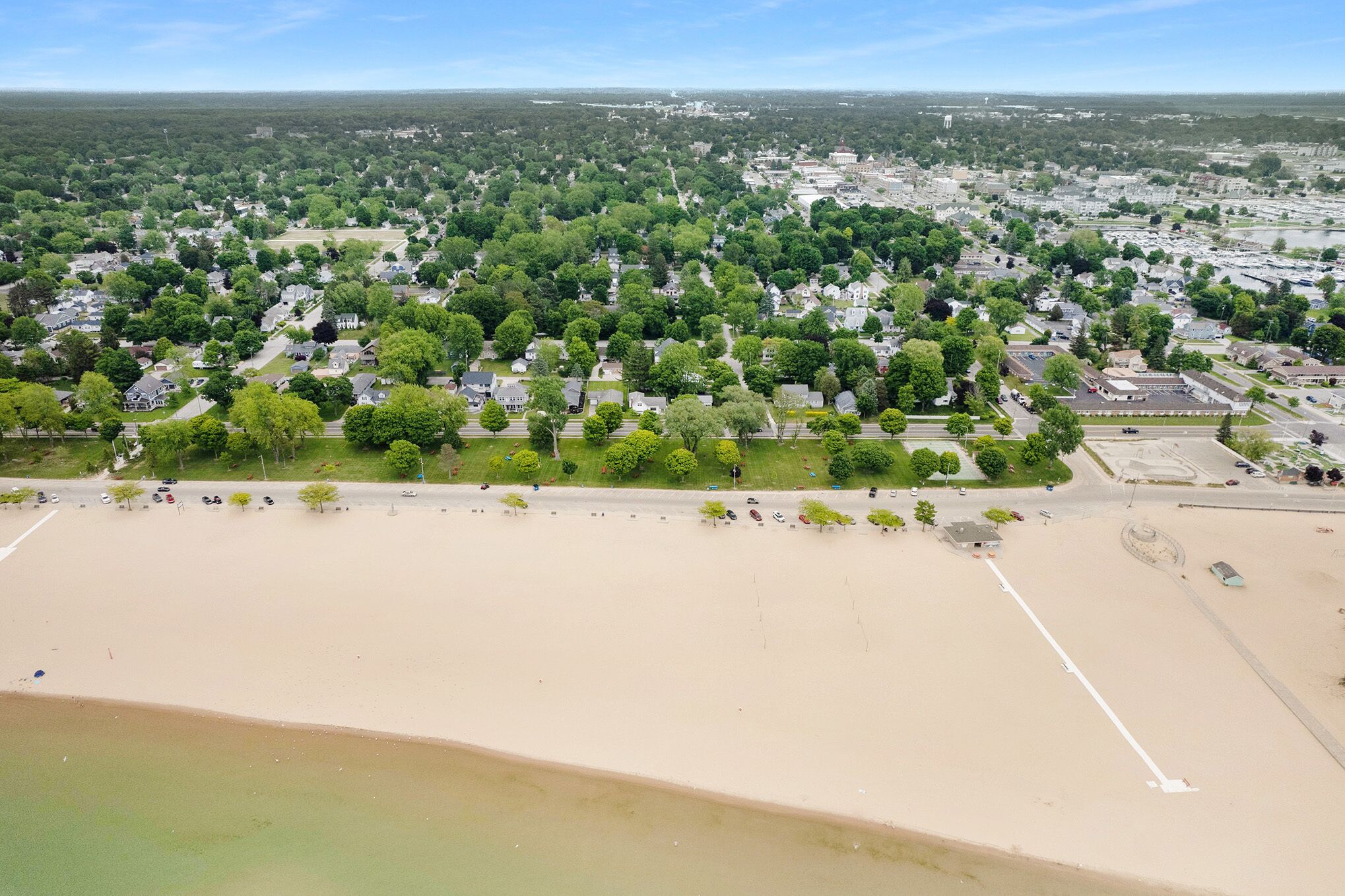 Vue aérienne d’un quartier résidentiel avec une plage de sable, des pelouses verdoyantes et des maisons.