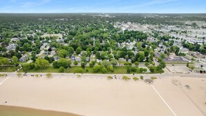 An aerial view of a residential area with a sandy beach, green lawns, and houses. - Lighthouse Cottage: 1 block from the beach, 2 blocks to downtown! (Ludington)