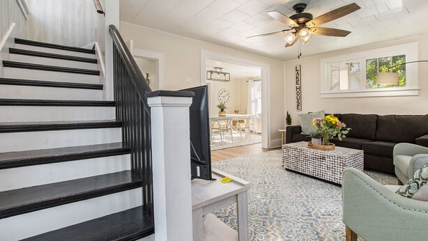 A staircase with black railings leading to a living area with a ceiling fan, a sofa, and a coffee table. - Lighthouse Cottage: 1 block from the beach, 2 blocks to downtown! (Ludington)