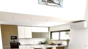 Una cocina moderna con armarios blancos, horno empotrado y comedor con mesa y sillas.