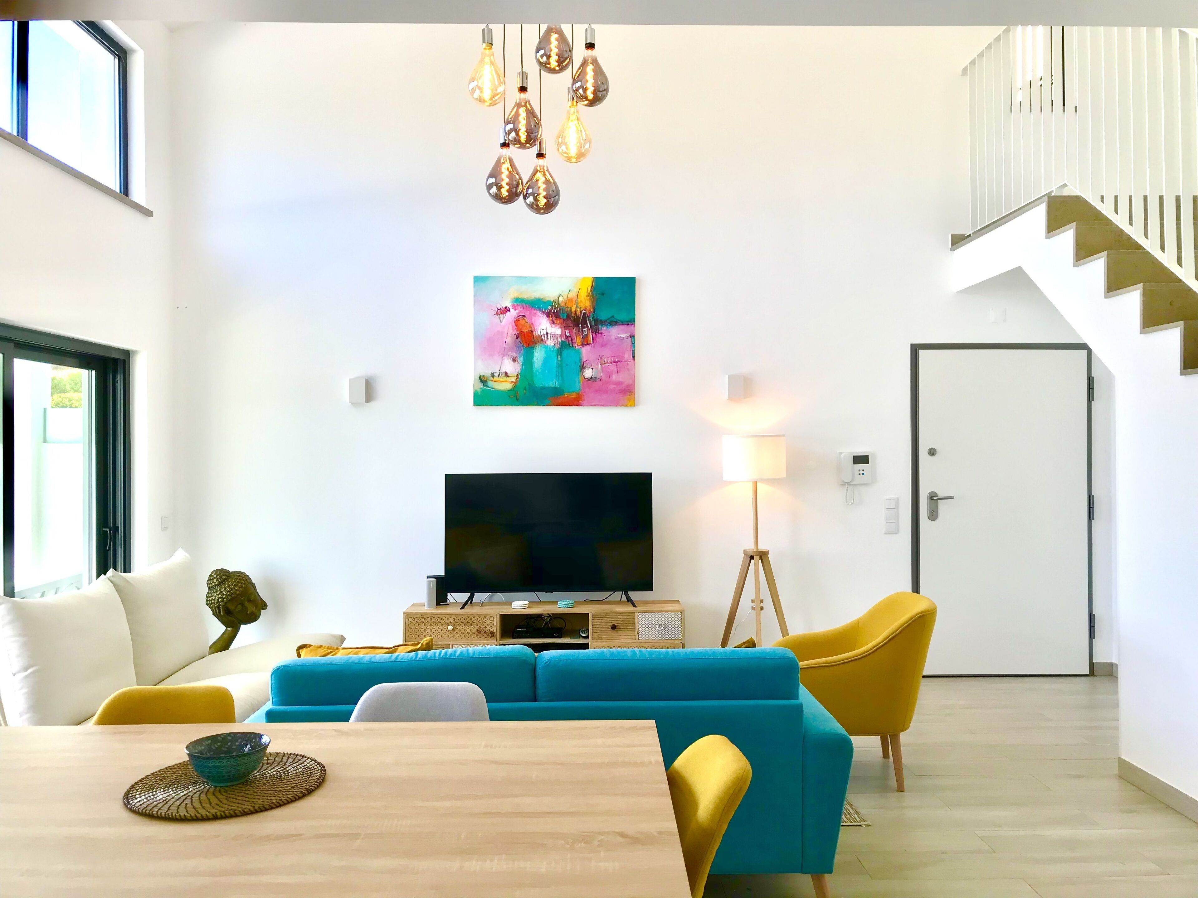Un salon moderne avec un canapé bleu, des fauteuils jaunes, une table à manger en bois et un téléviseur.