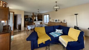 Ein Wohnzimmer mit blauem Sofa, gelber Decke und einem Essbereich mit Holzmöbeln.