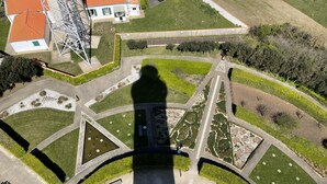 Eine Vogelperspektive auf eine angelegte Grünfläche mit geometrischen Gartenanlagen, Wegen und einem markanten Gebäudebau im Vordergrund.