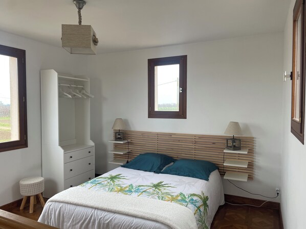 Um quarto com cama, mesas de cabeceira, guarda-roupa, janela e uma luminária no teto.